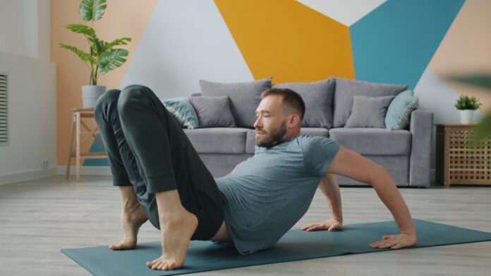 Man doing yoga on a mat in a living room.