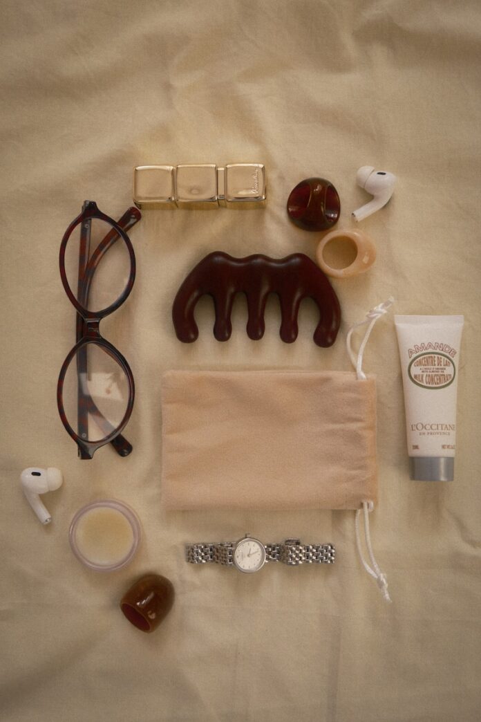 Eyeglasses, comb, lotion, watch, and earbuds arranged flat lay.